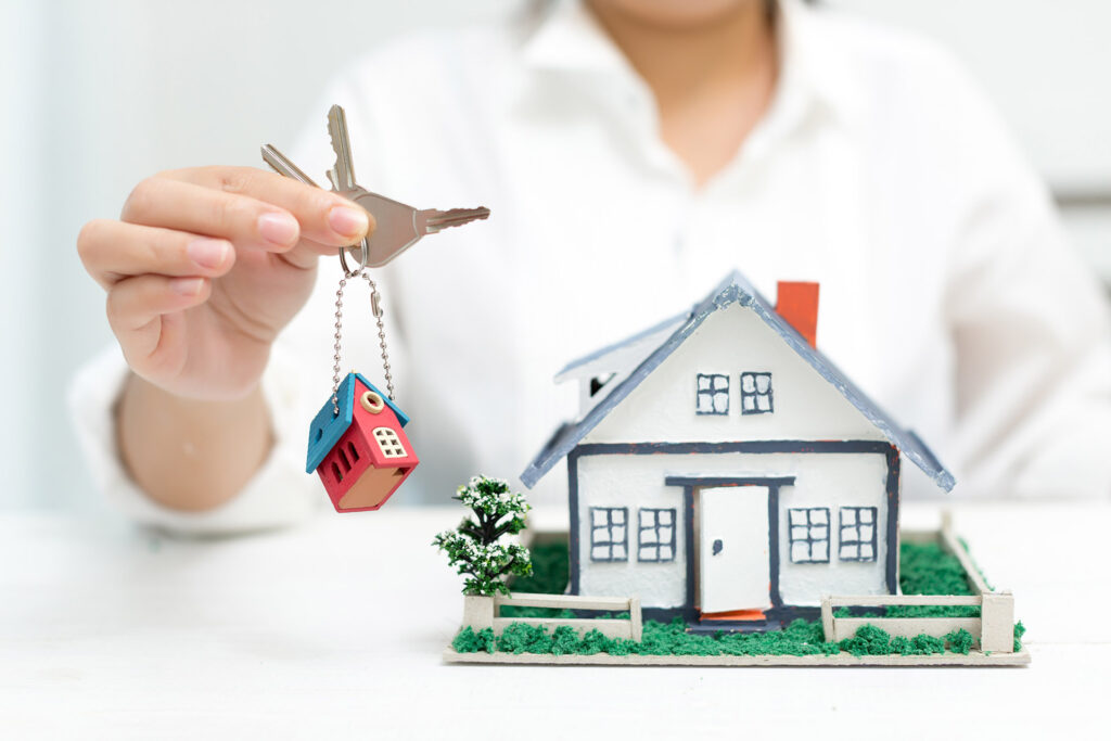 Person holding house keys beside miniature home model