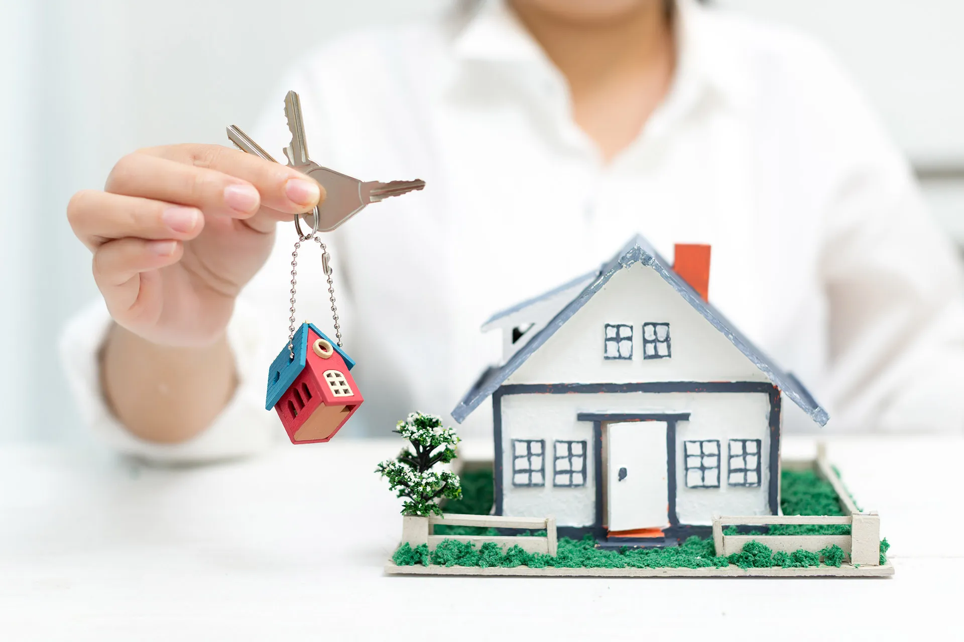 Person holding house keys beside miniature home model